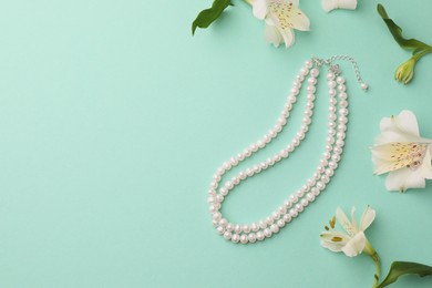 Photo of Elegant pearl necklace and beautiful flowers on turquoise background, flat lay. Space for text