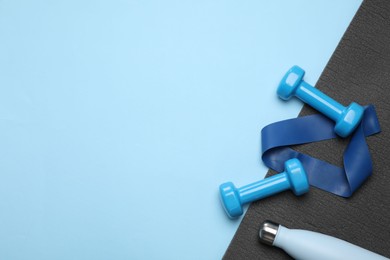 Photo of Two dumbbells, yoga mat, fitness elastic band and thermo bottle on light blue background, flat lay. Space for text