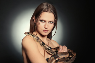 Photo of Beautiful woman with boa constrictor on dark background