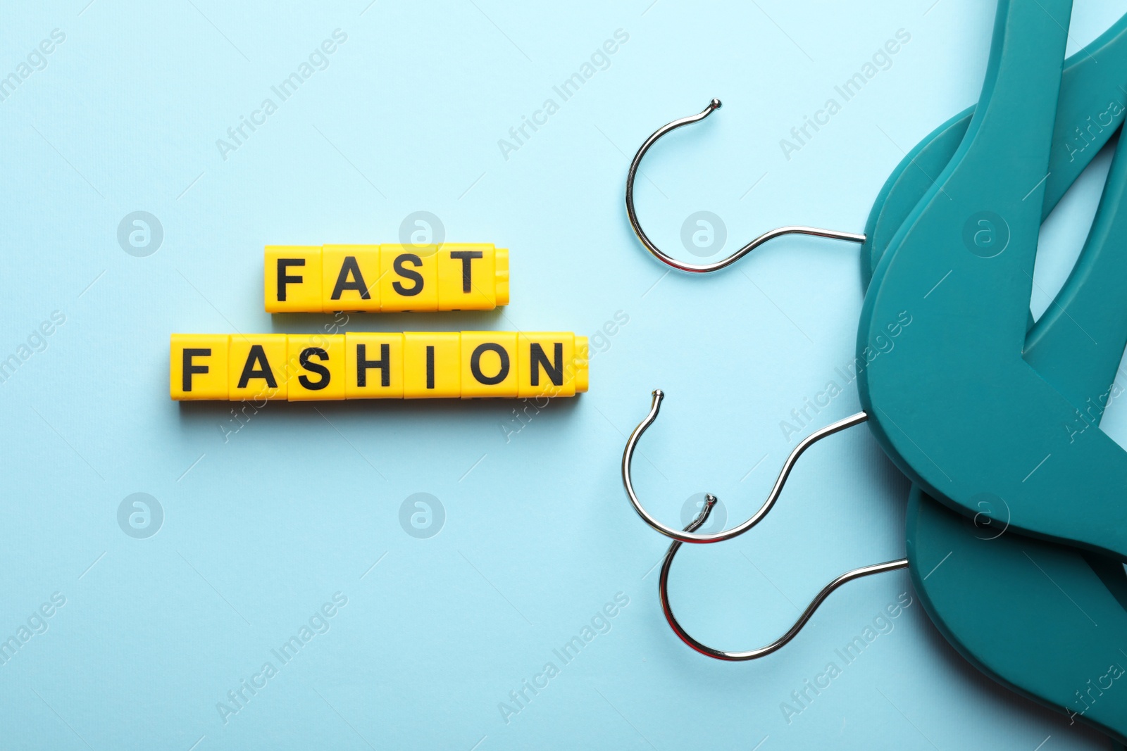 Photo of Yellow plastic cubes with phrase Fast Fashion and hanger on light blue background, flat lay