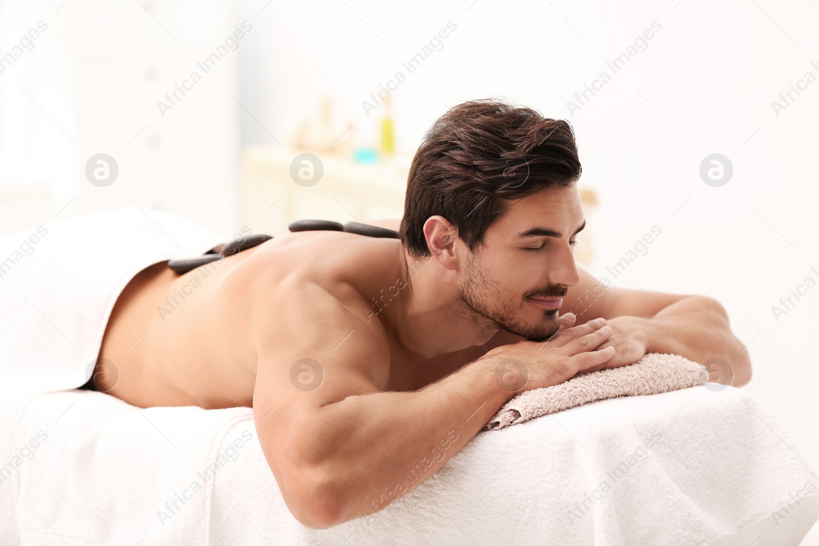 Photo of Handsome young man receiving hot stone massage in spa salon