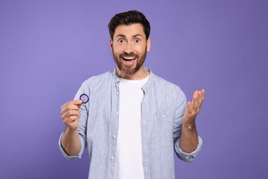 Photo of Emotional man holding condom on purple background. Safe sex