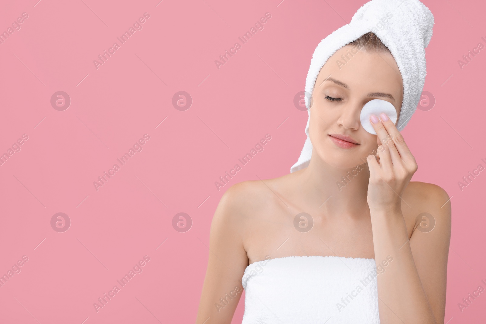 Photo of Young woman cleaning her face with cotton pad on pink background. Space for text