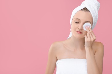 Photo of Young woman cleaning her face with cotton pad on pink background. Space for text