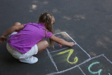 Little girl drawing hopscotch with chalk on asphalt outdoors. Happy childhood