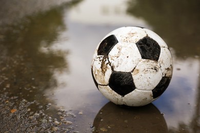 Photo of Dirty soccer ball near puddle outdoors, space for text