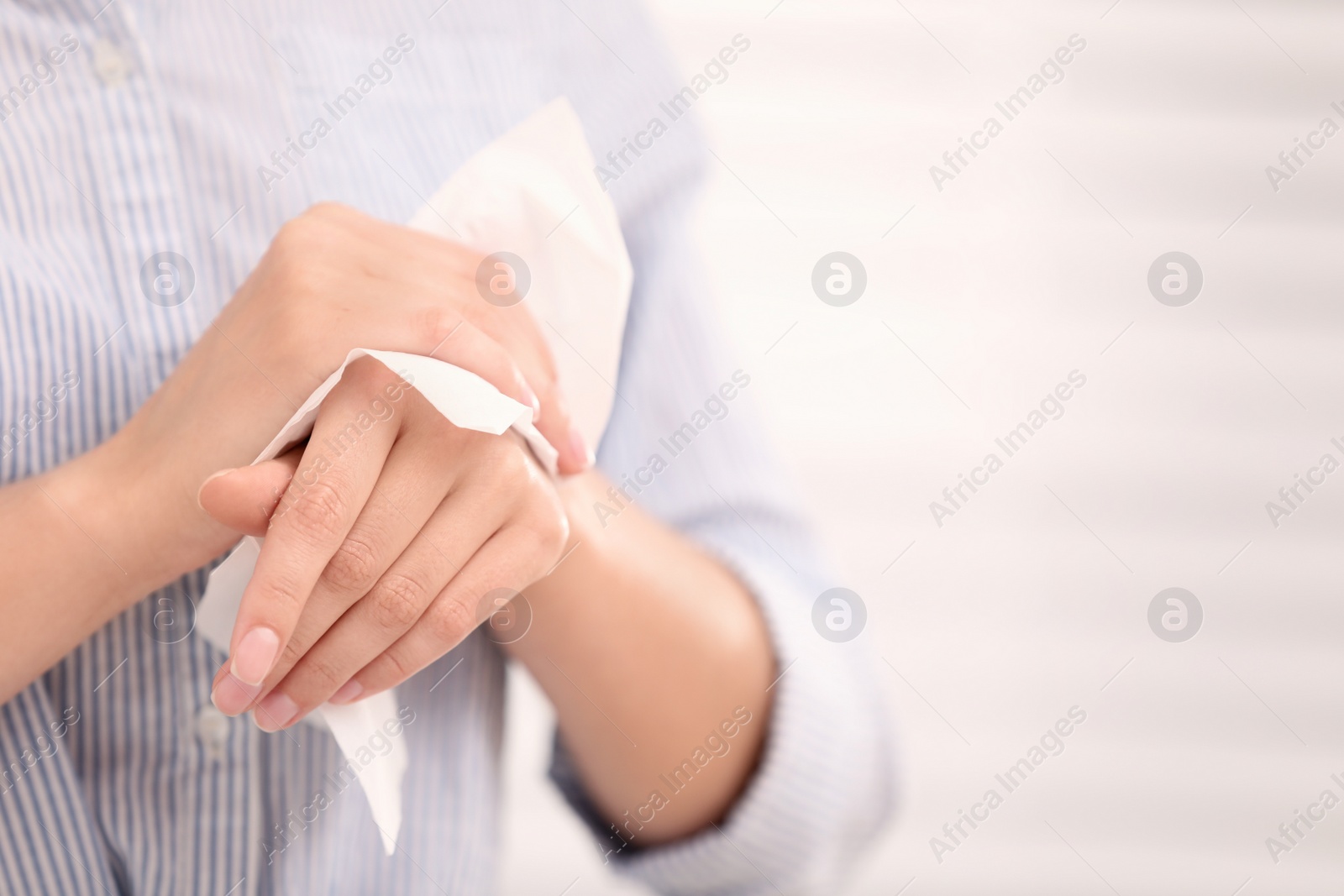 Photo of Woman cleaning hands with paper tissue on light background, closeup