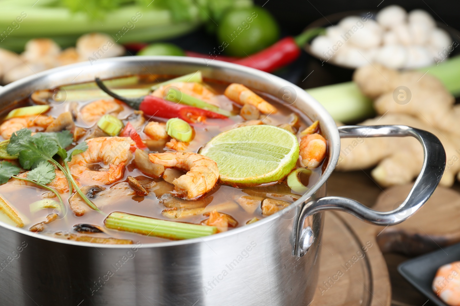 Photo of Saucepan with delicious Tom Yum soup and ingredients on table, closeup