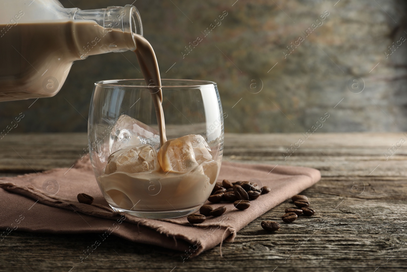 Photo of Pouring coffee cream liqueur into glass at wooden table, closeup