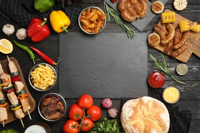 Photo of Flat lay composition with barbecued meat and vegetables on black wooden table. Space for text