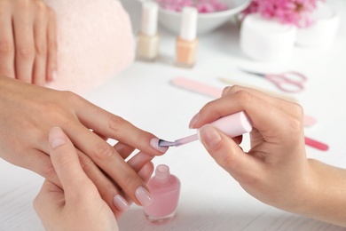 Manicurist applying polish on client's nails at table, closeup. Spa treatment