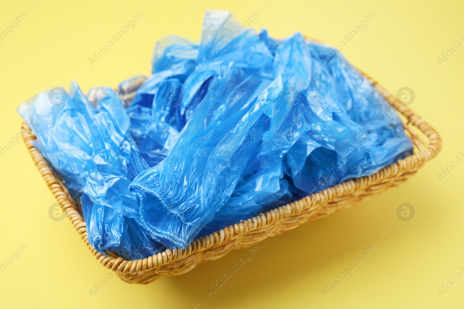 Photo of Blue medical shoe covers in wicker basket on yellow background, closeup