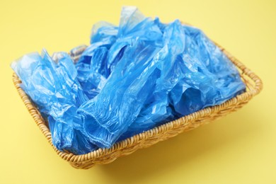 Blue medical shoe covers in wicker basket on yellow background, closeup