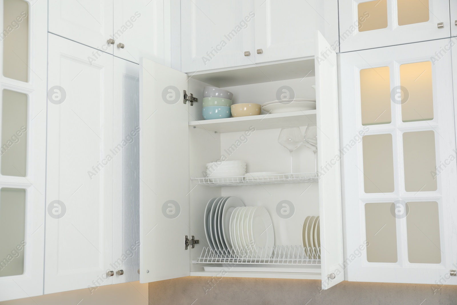 Photo of Clean plates, bowls and glasses on shelves in cabinet indoors