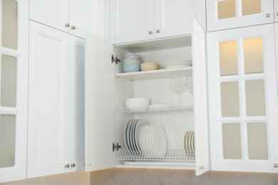 Clean plates, bowls and glasses on shelves in cabinet indoors