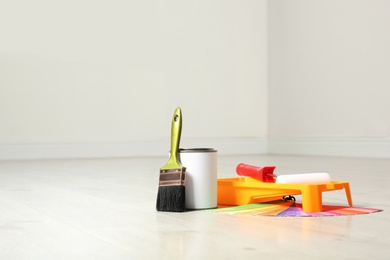 Can of paint and decorator tools on wooden floor indoors. Space for text