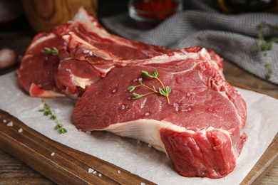 Photo of Fresh raw beef cut with thyme and salt on wooden table, closeup