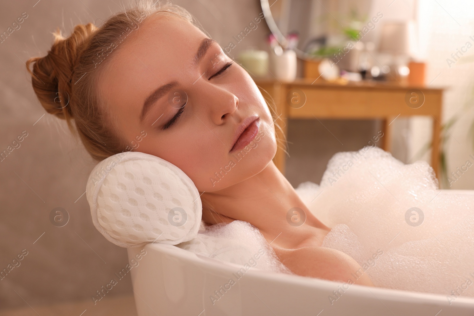 Photo of Young woman using pillow while enjoying bubble bath indoors