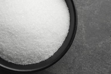 Photo of Granulated sugar in bowl on grey textured table, top view. Space for text