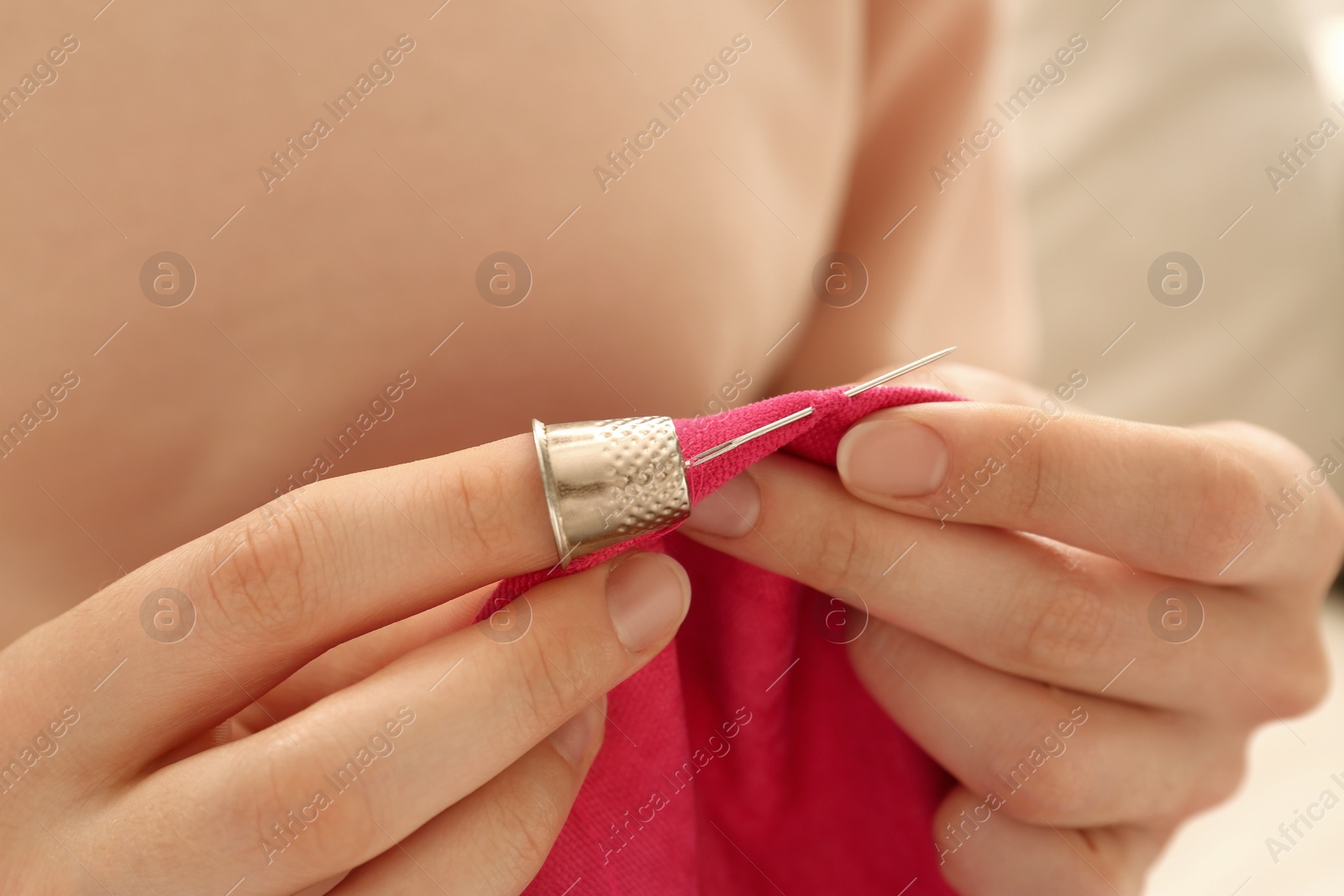 Photo of Woman sewing on red fabric with thimble and needle, closeup