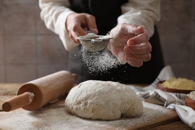 Photo of Woman sprinkling flour over dough at wooden table, closeup