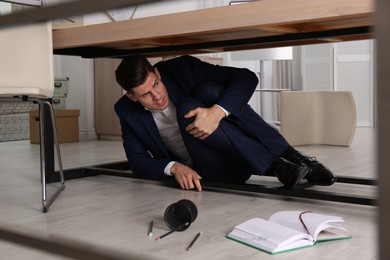 Photo of Scared man hiding under office desk during earthquake