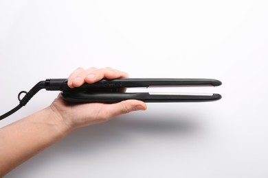 Photo of Woman holding flat hair iron on white background, closeup