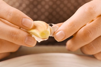 Woman peeling fresh garlic at table, selective focus