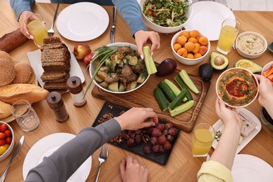 Friends eating vegetarian food at wooden table indoors, closeup