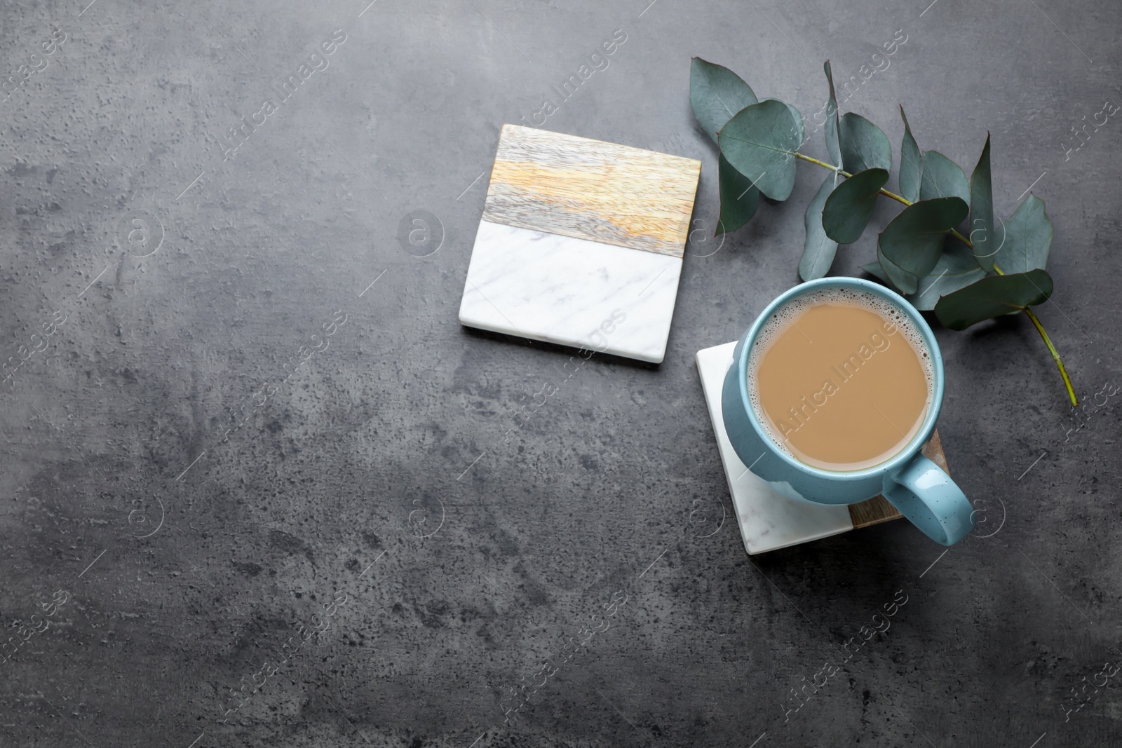 Photo of Mug of coffee, stylish cup coasters and eucalyptus branch on grey table, flat lay. Space for text