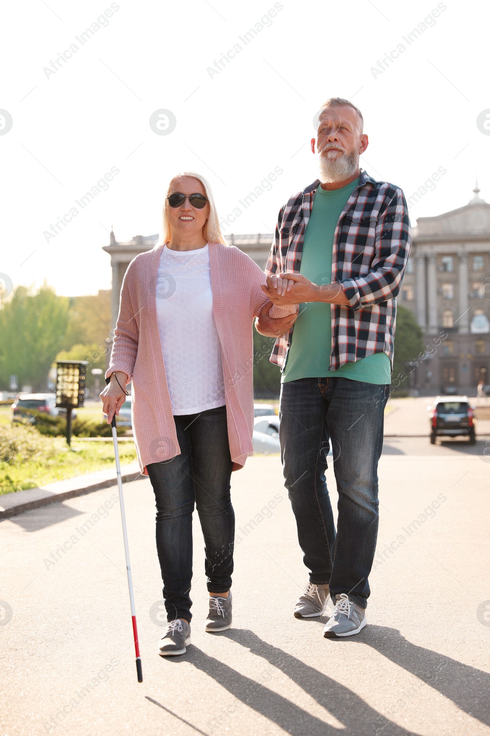 Photo of Mature man helping blind person with long cane walking outdoors