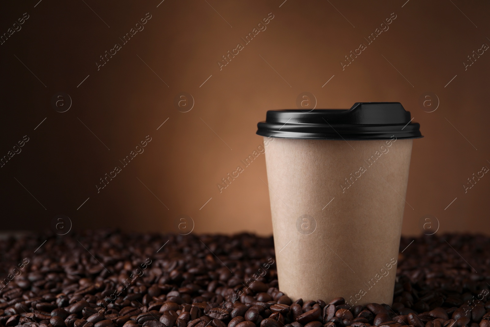 Photo of Coffee to go. Paper cup on roasted beans against brown background, space for text