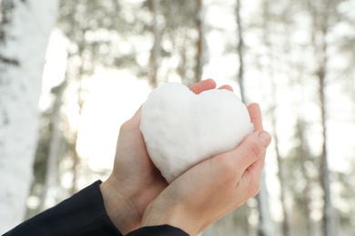 Photo of Woman holding heart made of snow outdoors, closeup