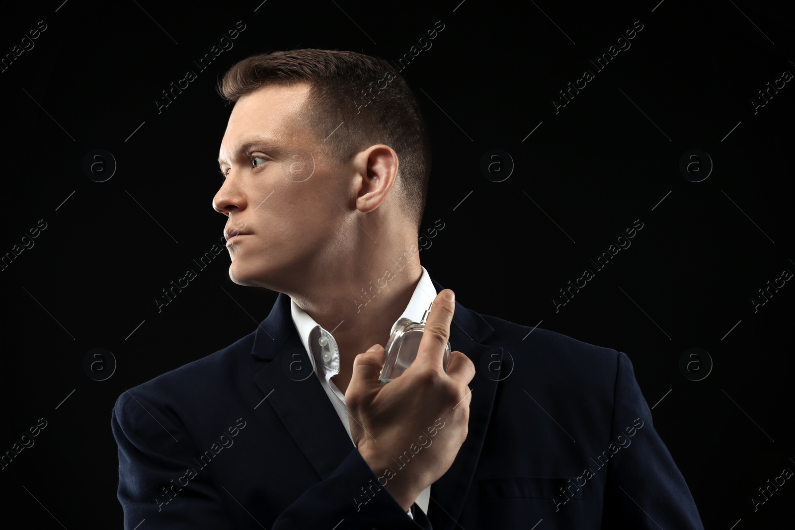 Photo of Handsome man in suit using perfume on black background