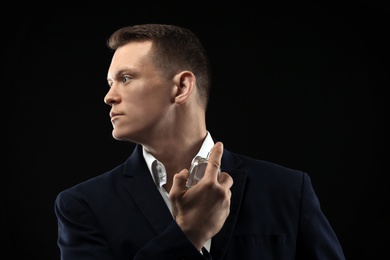 Photo of Handsome man in suit using perfume on black background