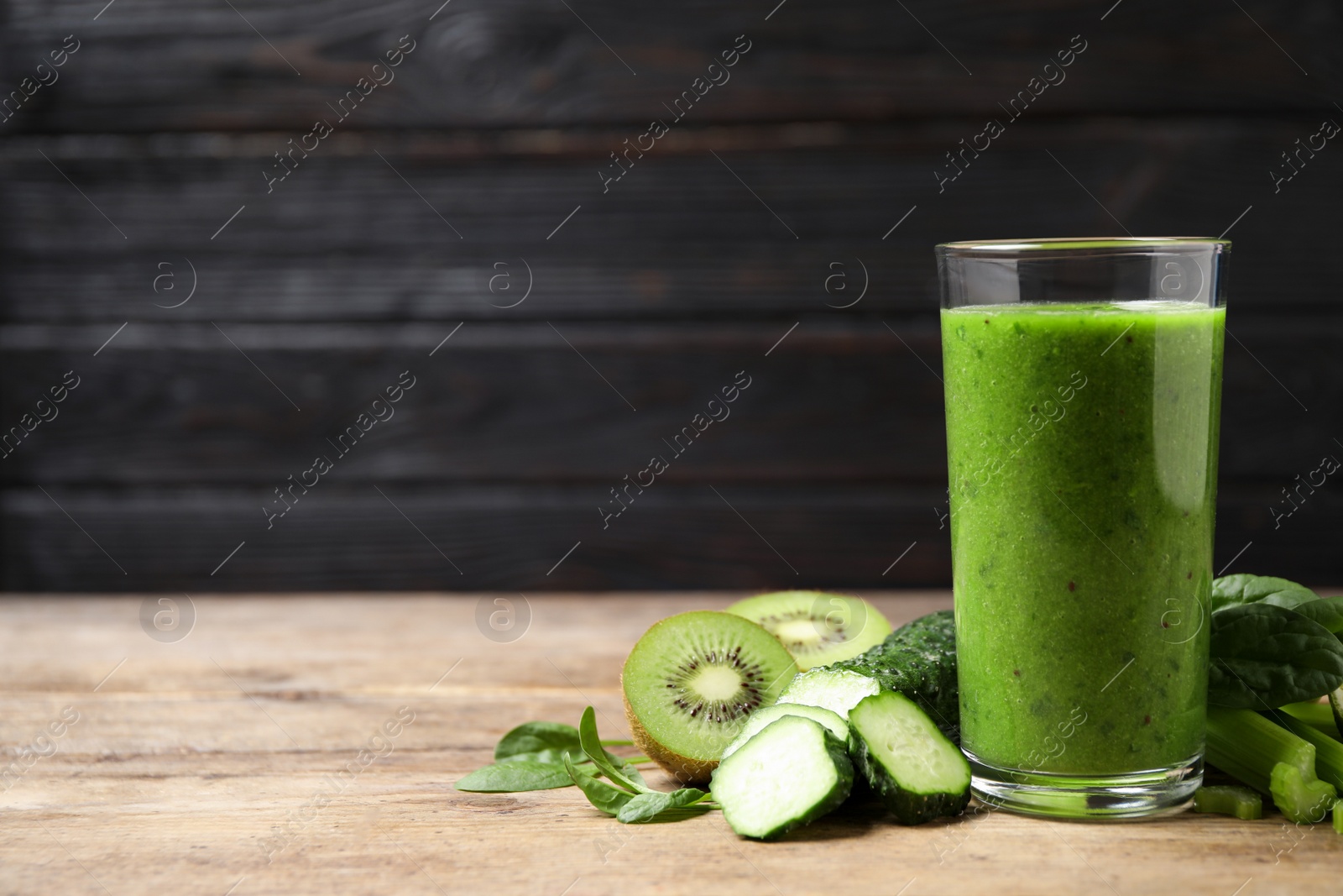 Photo of Delicious green juice and fresh ingredients on wooden table against black background. Space for text