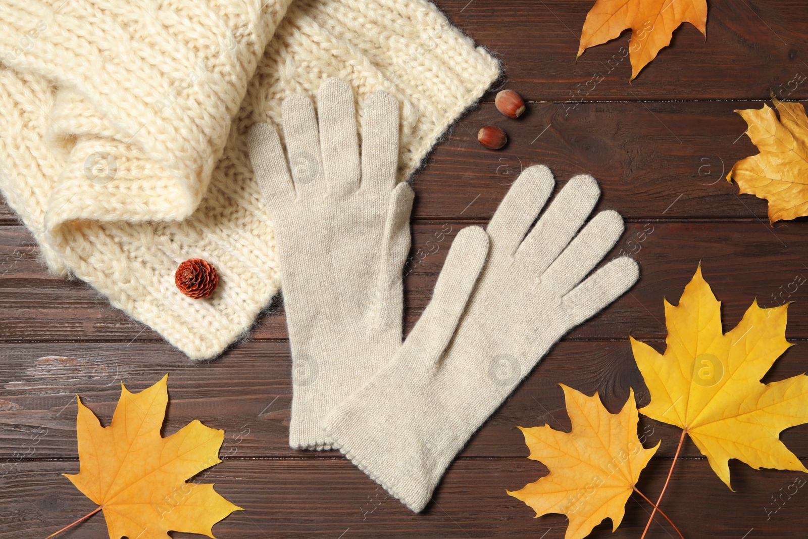 Photo of Stylish white woolen gloves, scarf and dry leaves on wooden table, flat lay