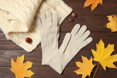 Photo of Stylish white woolen gloves, scarf and dry leaves on wooden table, flat lay