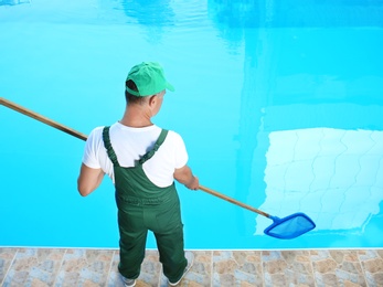 Male worker cleaning outdoor pool with scoop net