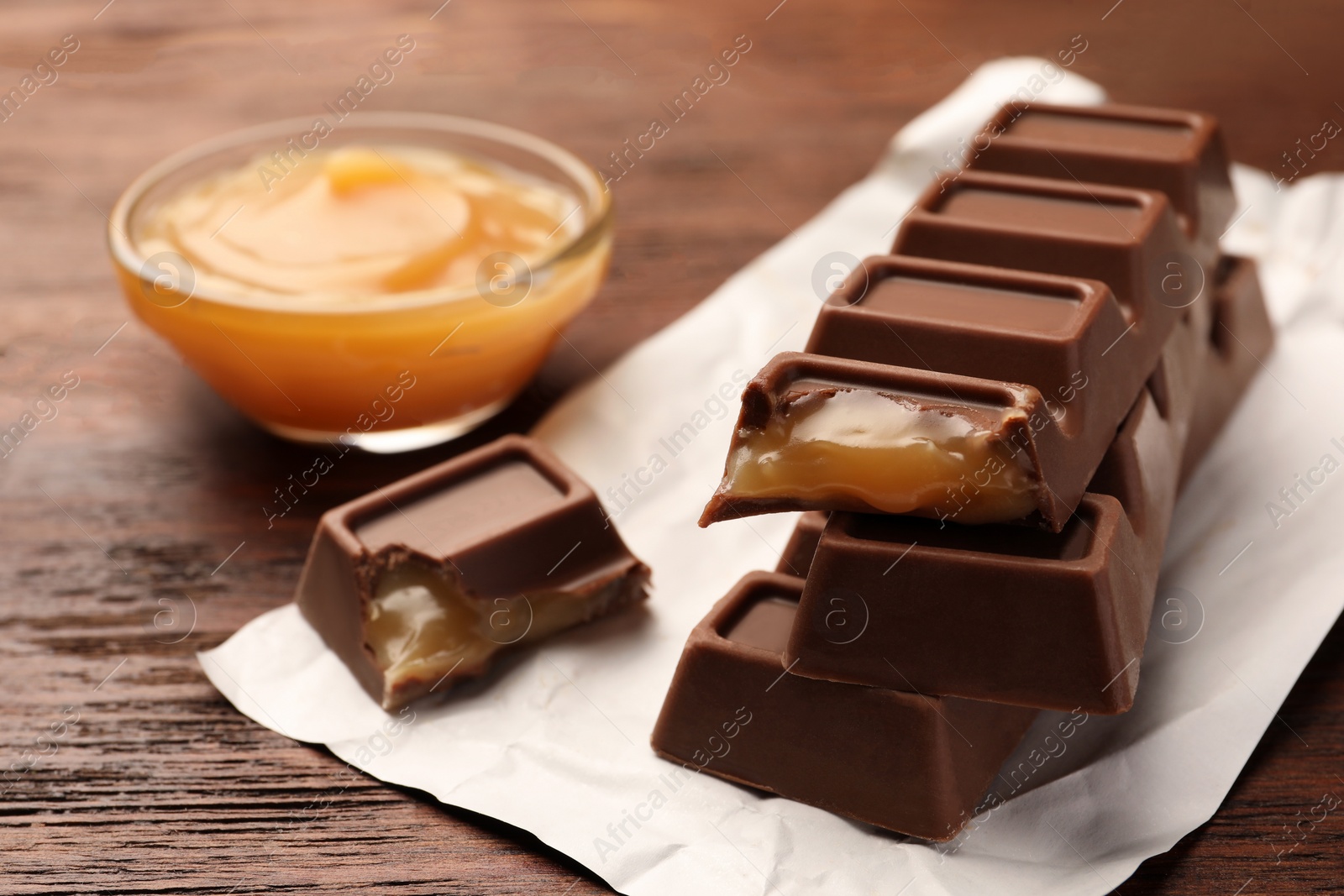 Photo of Tasty chocolate bars and bowl of caramel on wooden table, closeup. Space for text