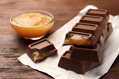 Tasty chocolate bars and bowl of caramel on wooden table, closeup. Space for text