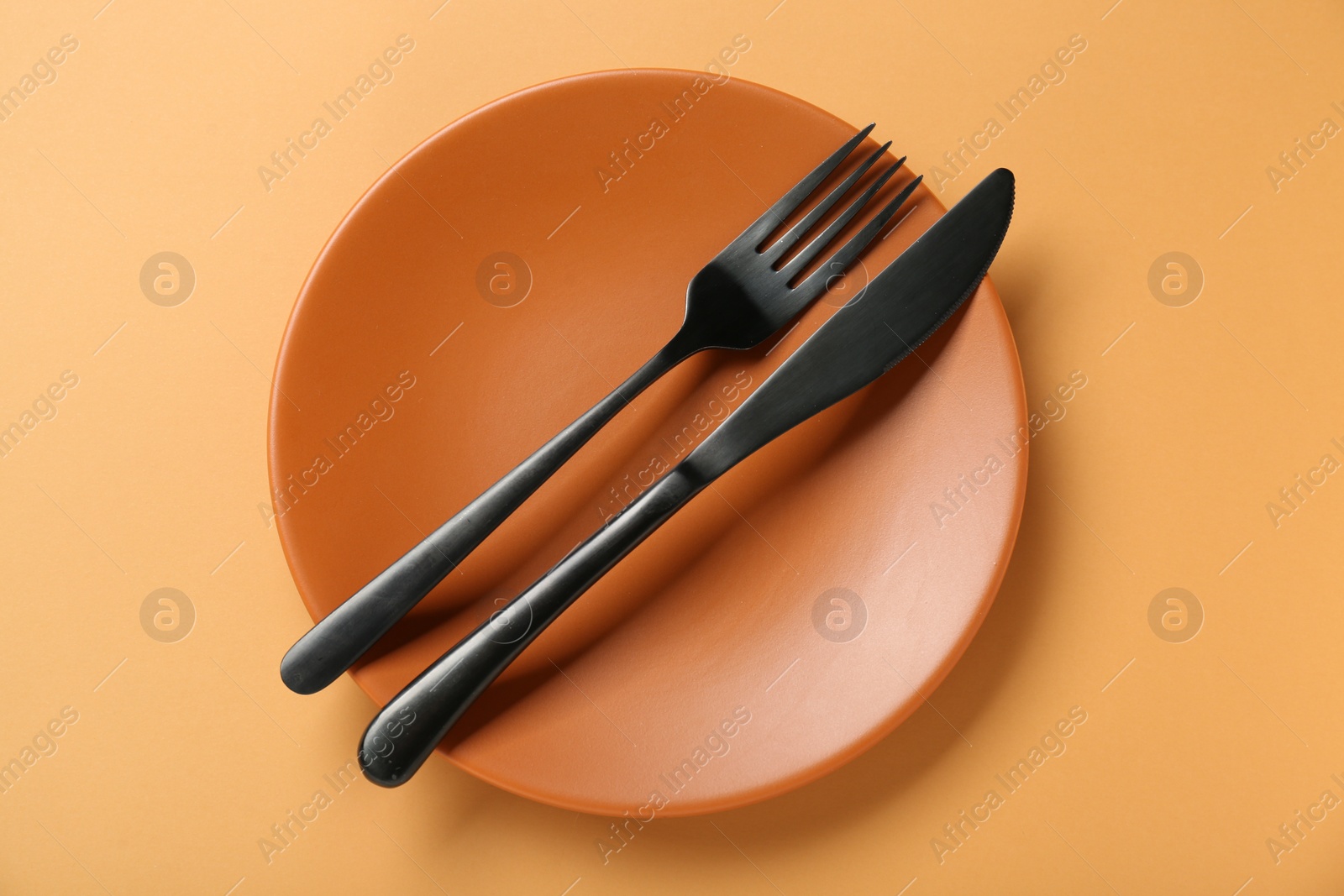 Photo of Ceramic plate with cutlery on pale orange background, top view