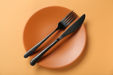 Ceramic plate with cutlery on pale orange background, top view