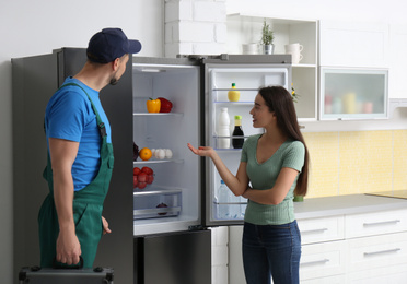 Male technician talking with client near refrigerator in kitchen