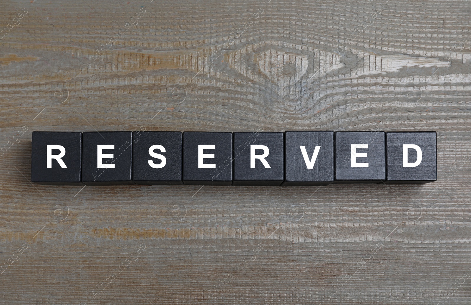 Photo of Word RESERVED made with cubes on wooden surface, top view. Table setting element