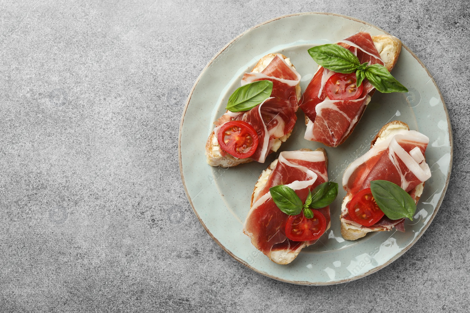 Photo of Tasty sandwiches with cured ham, basil and tomatoes on grey table, top view. Space for text