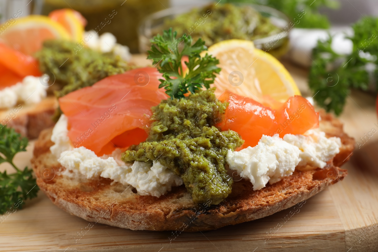 Photo of Delicious bruschetta with cream cheese, salmon and pesto sauce on wooden board, closeup