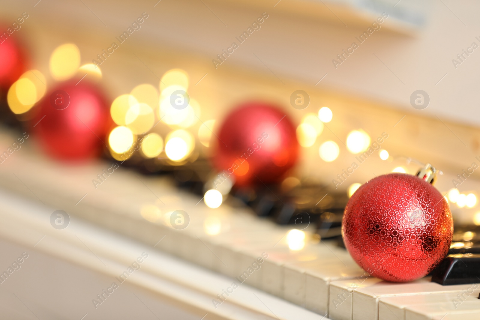 Photo of Red bauble and fairy lights on piano keys, space for text. Christmas music