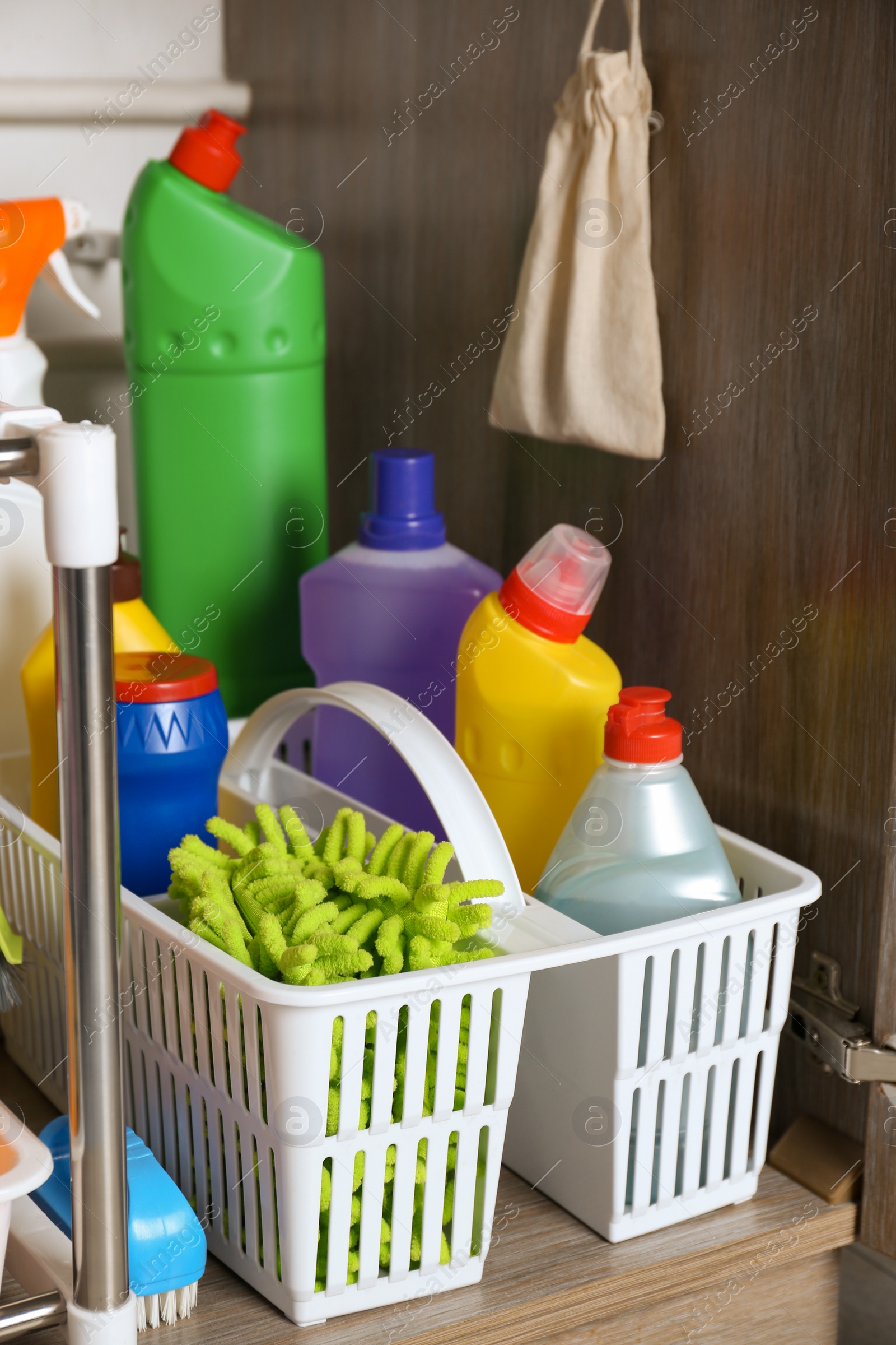 Photo of Open under sink cabinet with different cleaning supplies in kitchen