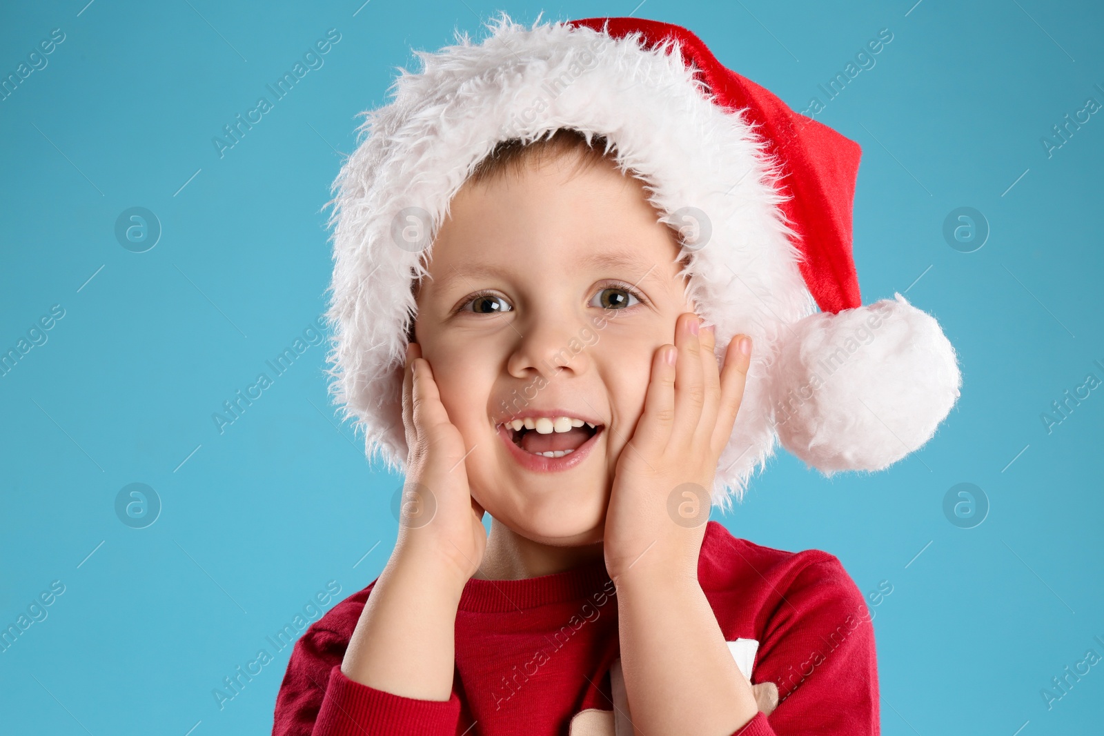 Photo of Cute child in Santa hat on light blue background. Christmas celebration